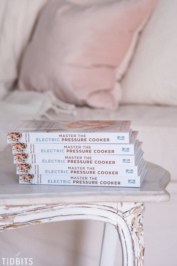 A stack of books on a table 'Master The Electric Pressure Cooker Cookbook'