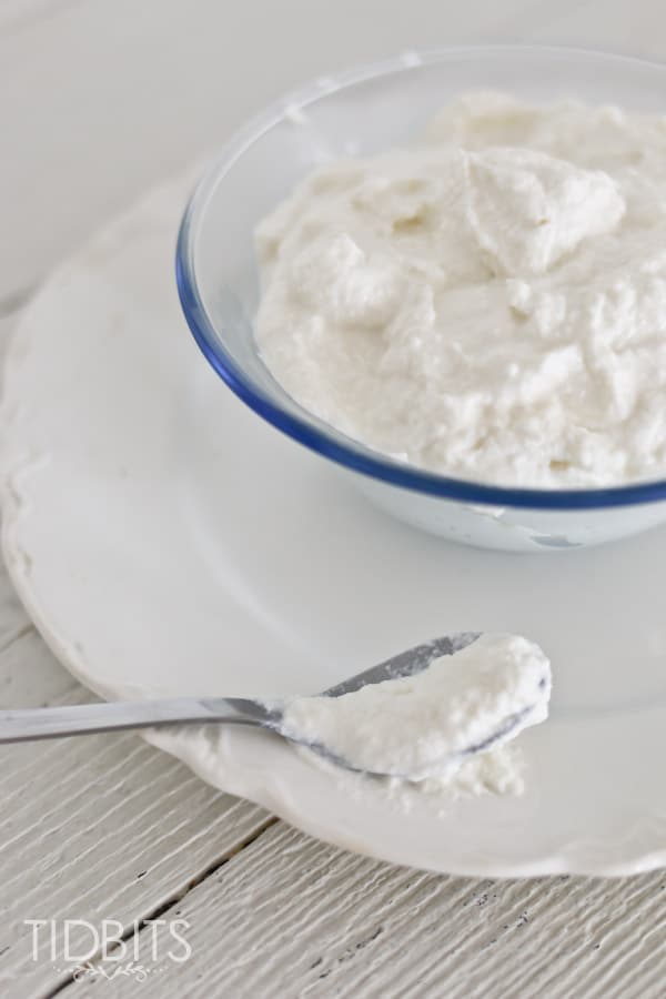 A spoon full of ricotta cheese next to a glass bowl