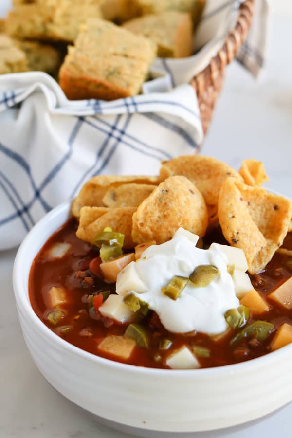 chili in a white bowl topped with sour cream, chips and cheese