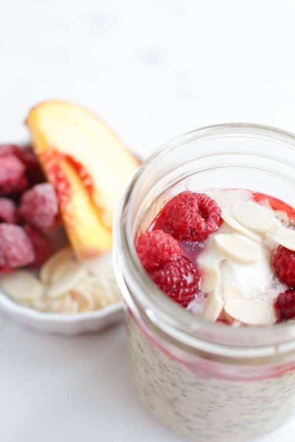 Mason jar steel cut oats with peaches and raspberries and cream on top