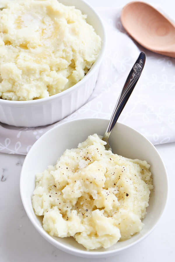 Mashed potato in two white bowls with a serving spoon