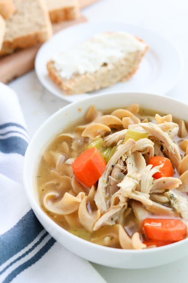A bowl of chicken noodle soup with bread in the background