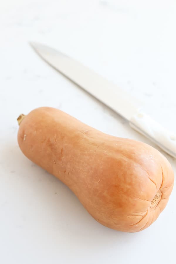 Butternut squash on a white surface with a knife