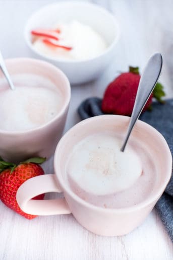 Instant Pot Strawbery Crio Bru in a pink cup with cream on a wood board with strawberries