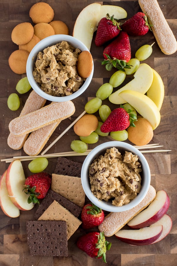 White bowls filled with healthy cookie dough surrounded by fruit and crackers