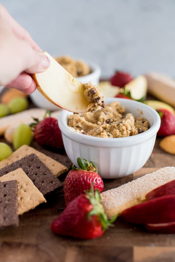 White bowls filled with healthy cookie dough surrounded by fruit and crackers