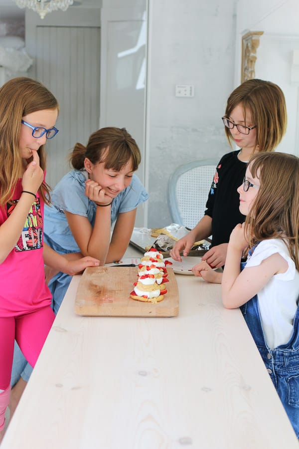 four girls looking at strawberry shortcakes on a wood board