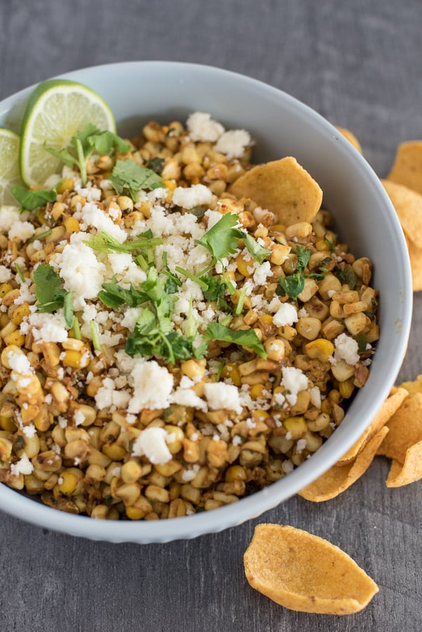 Large bowl of Mexican Street Corn Salad with cheese and lime wedges