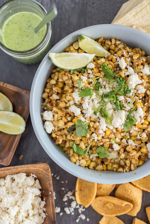 Mexican Street Corn Salad topped with cheese and lime wedges in a bowl