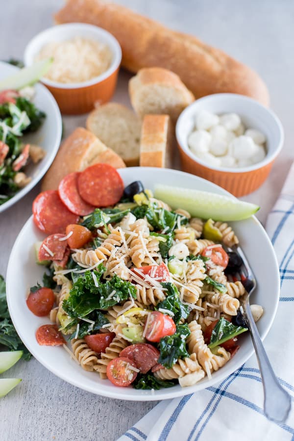 pasta salad with olives, pepperoni, cheese, kale, and cucumber in a white bowl