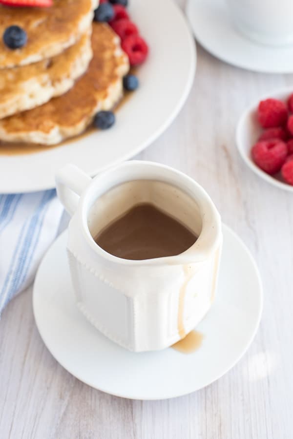 Cinnamon Syrup in a white cup on a white plate with pancakes in the background