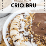 Chocolate Crio Bru Smoothie in a white bowl topped with bananas and shaved chocolate