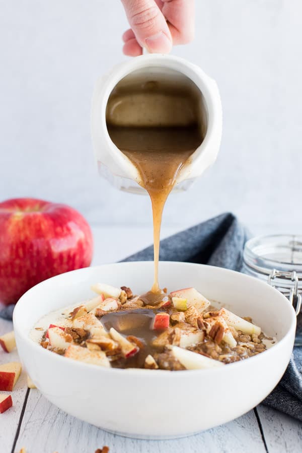 syrup pouring over a white bowl of apple oatmeal