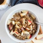 white bowl of steel cut oats with apples cinnamon and syrup