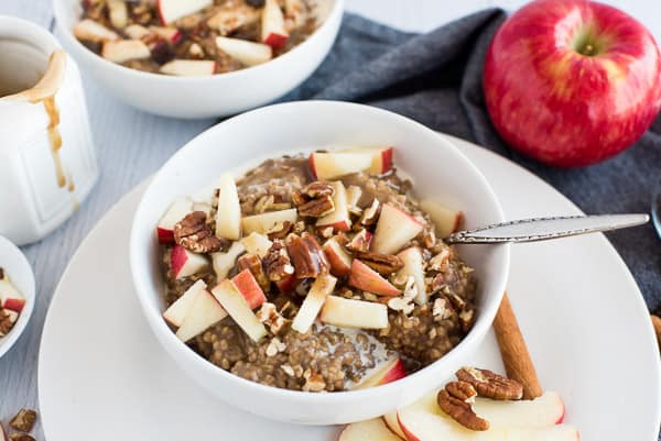 white bowl of steel cut oats with apples cinnamon and syrup