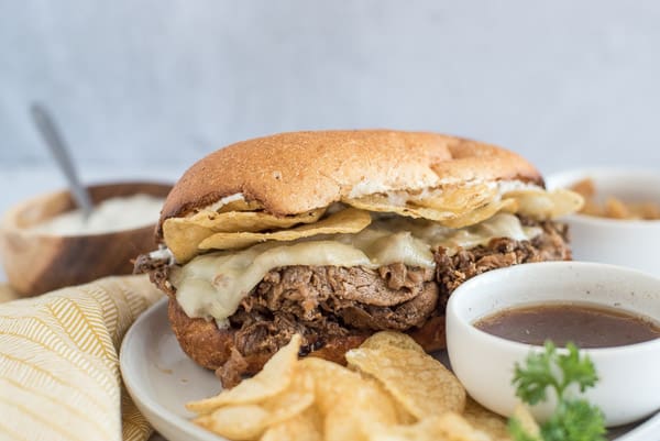 French dip sandwich on a plate with chips and horseradish sauce