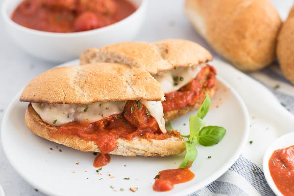 meatball sandwich cut in half on a white plate with basil