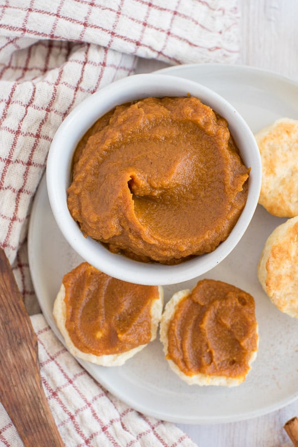 pumpkin butter in a white bowl with a spoon and biscuits on the side
