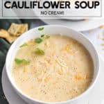 instant pot cauliflower soup in a white bowl with cheese and herbs