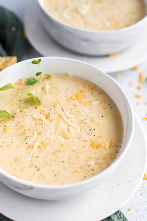 instant pot cauliflower soup in a white bowl with cheese and herbs