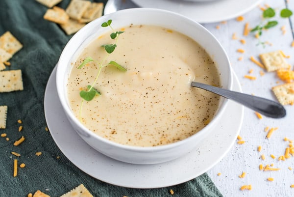 instant pot cauliflower soup in a white bowl with cheese and herbs and a green napkin