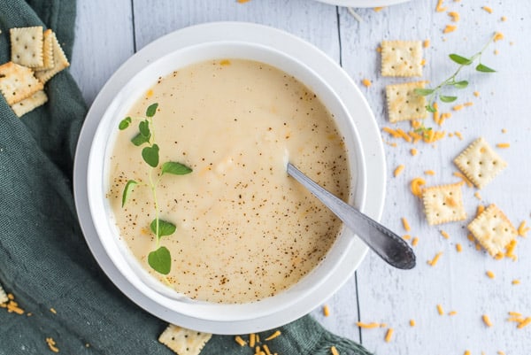 instant pot cauliflower soup in a white bowl with cheese and herbs and a spoon