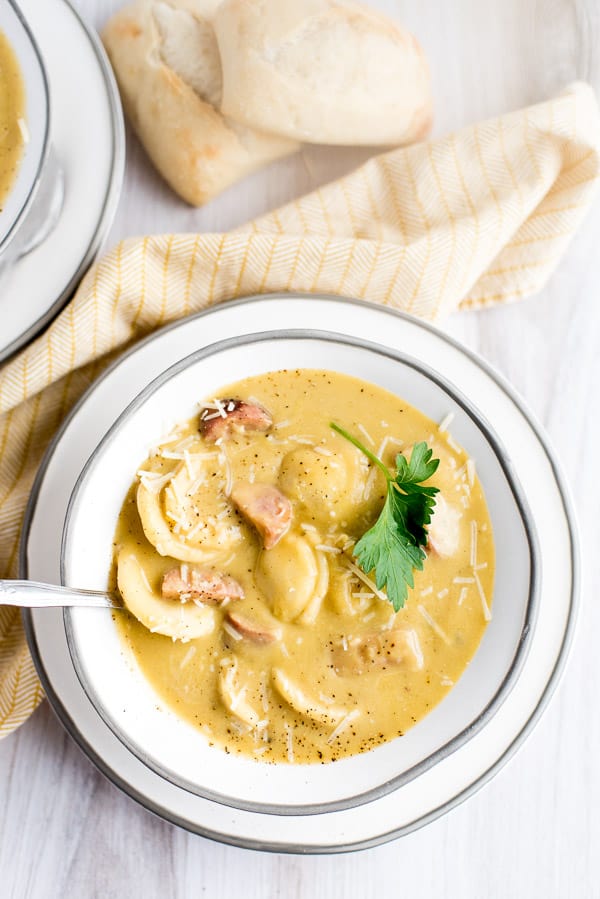 butternut squash soup with ravioli and sausage in a white bowl with a spoon