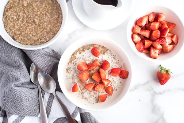 bowl of steel cut oatmeal with strawberries and cream and a cup of chocolate