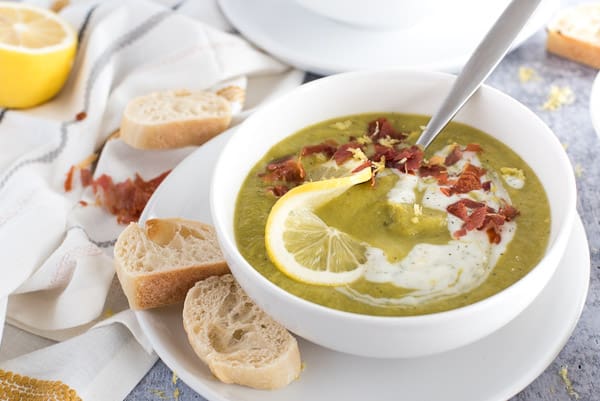 Green asparagus soup with yogurt, bacon, and a lemon slice in a white bowl