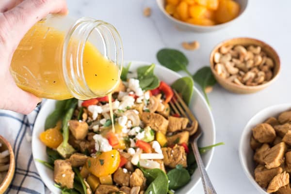 orange vinaigrette pouring into a spinach salad with chicken, oranges, bell peppers and nuts