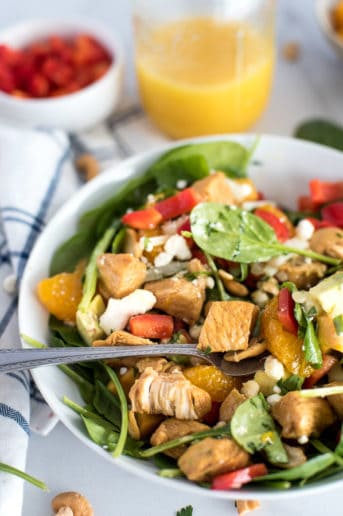 bowl of spinach salad with chicken, bell peppers, mandarin oraanges, and cheese