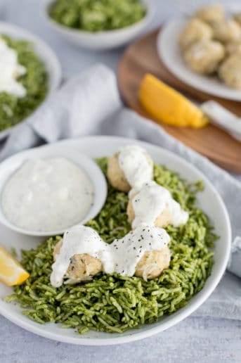 White bowl of green rice and chicken ricotta meatballs covered in a white sauce