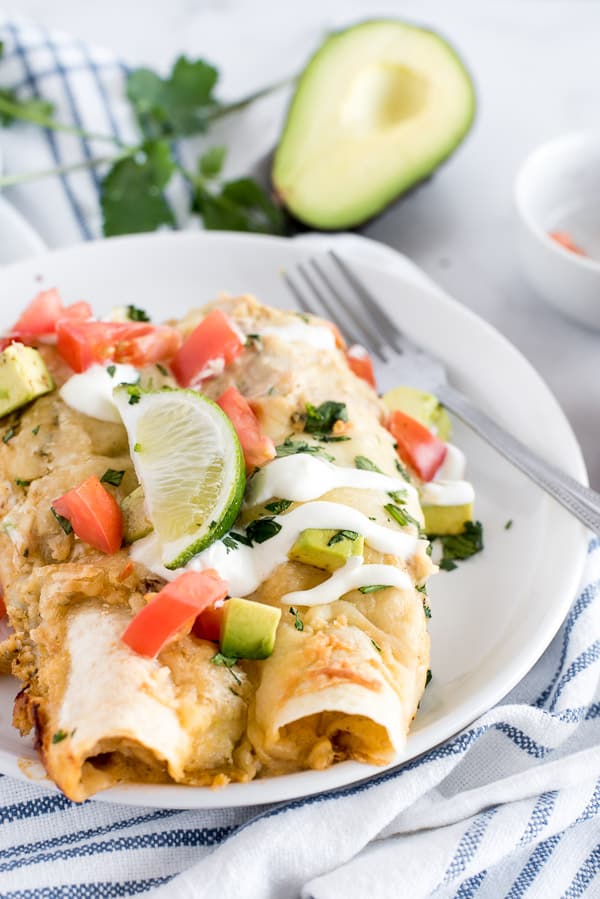 2 chicken enchiladas on a white plate with avocados and tomatoes