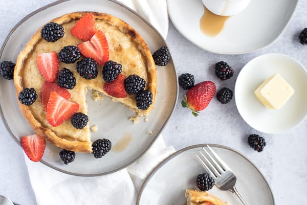 Giant pancake with a slice on a white plate with berries