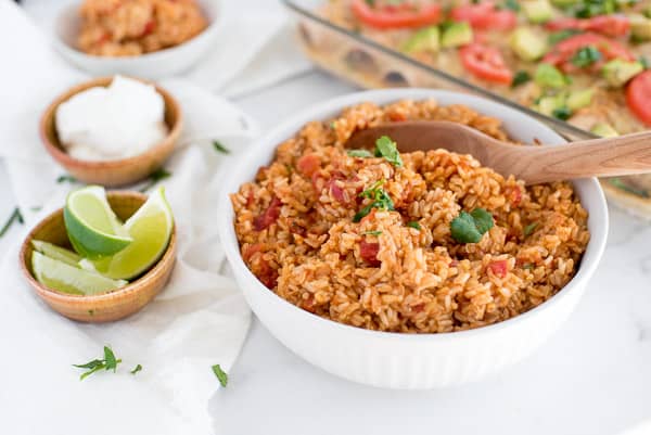 mexican rice with tomatoes in a white dish with a wood spoon