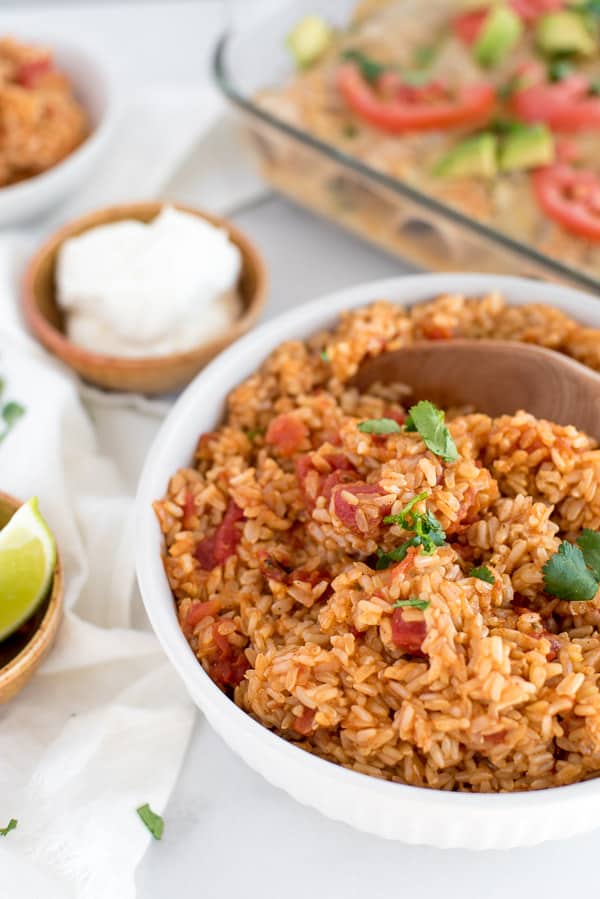 mexican rice with tomatoes in a white dish with a wood spoon