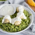 White bowl of green rice and chicken ricotta meatballs covered in a white sauce