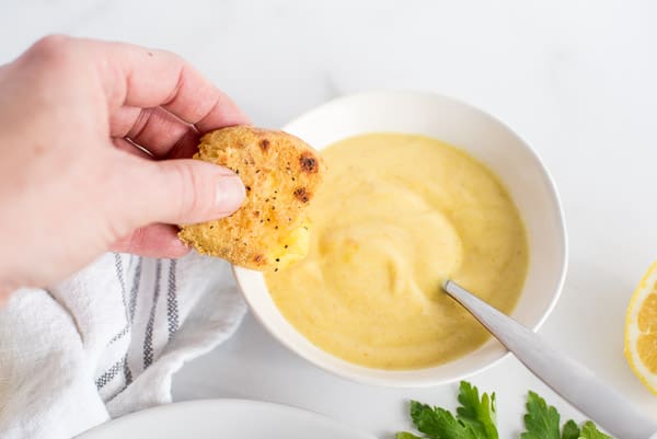 bowl of lemon dipping sauce with a hand dipping a smashed potato