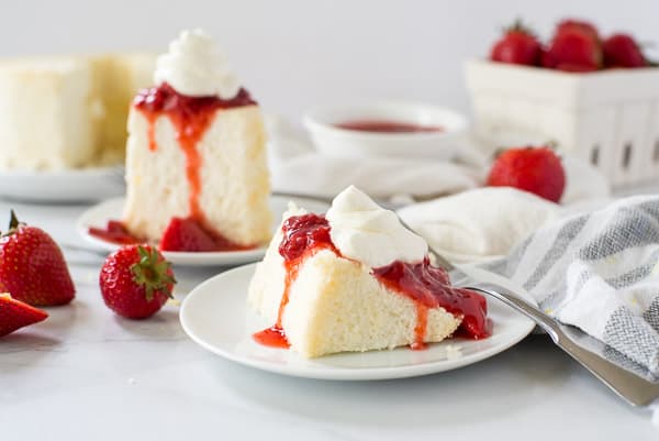 two slices of angel food cake on a white plate with strawberries and whipped cream