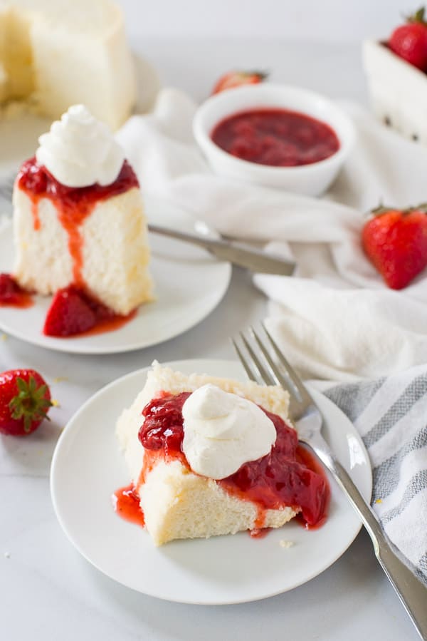 two slices of angel food cake on a white plate with strawberries and whipped cream