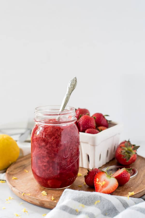strawberry jam in a mason jar next to sliced strawberries on a cutting board