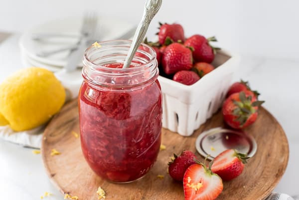 strawberry jam in a mason jar next to sliced strawberries on a cutting board