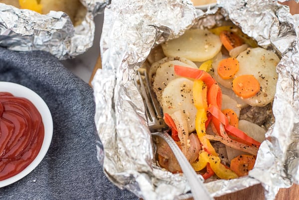 potatoes, peppers, carrots, and onions in a tinfoil packet with sauce on the side