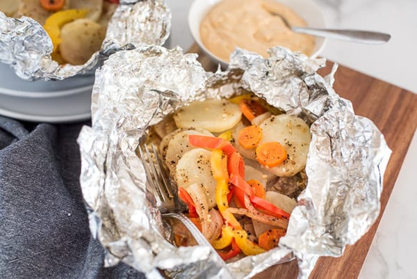 potatoes, peppers, carrots, and onions in a tinfoil packet with sauce on the side