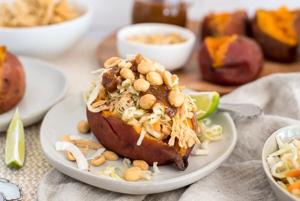 sweet potato on a white plate filled with coleslaw, peanuts, and peanut sauce