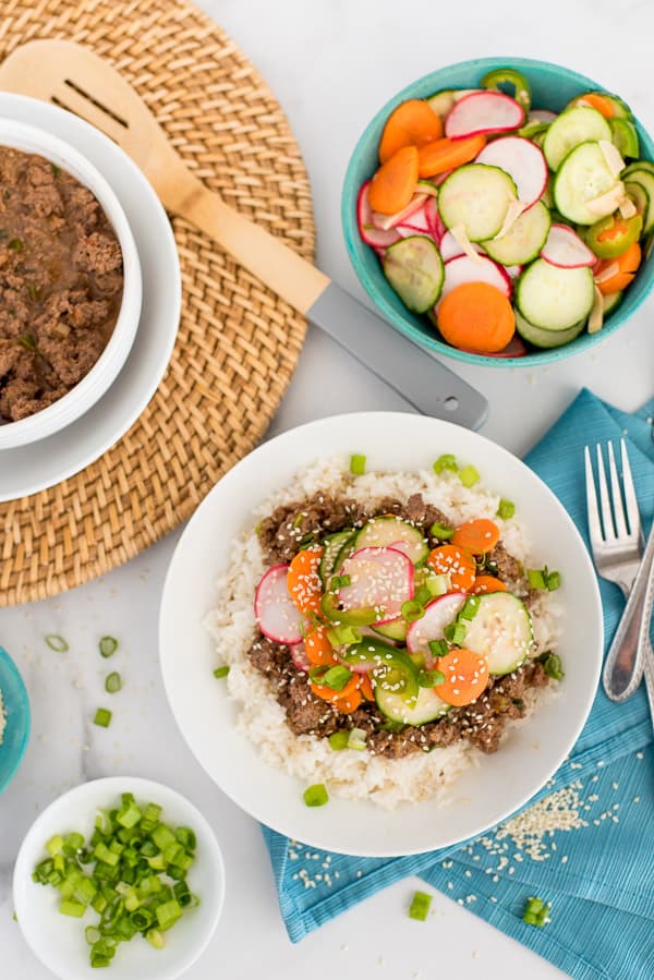 Korean Beef topped with radishes, carrots, and cucumbers in a white bowl of rice