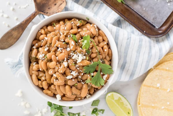 White bowl with beans, cilantro and lime with a sprinkle of cotija cheese
