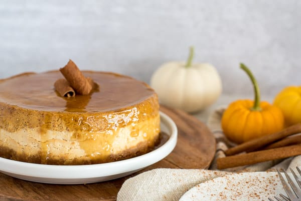 Whole pumpkin cheesecake sitting on a white plate with pumpkins on side