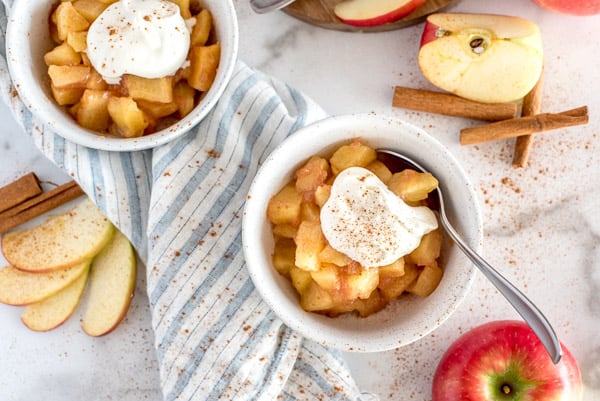 white bowl of cinnamon spiced apples topped with cream and cinnamon