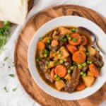 Bowl of beef stew with carrots, peas and onions in a white bowl